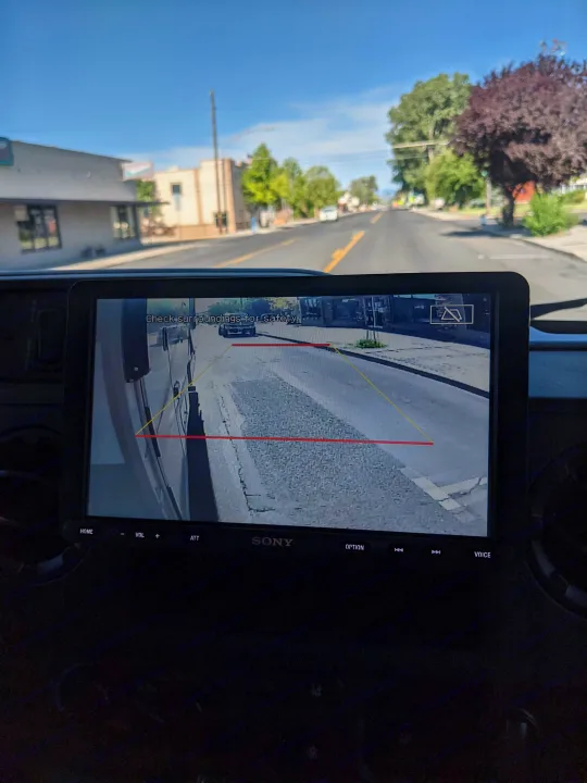 Inside an RV rental, the dashboard screen shows a rearview camera view with parking lines. A bright street is visible ahead.. Winnebago Minnie Winnie 2022