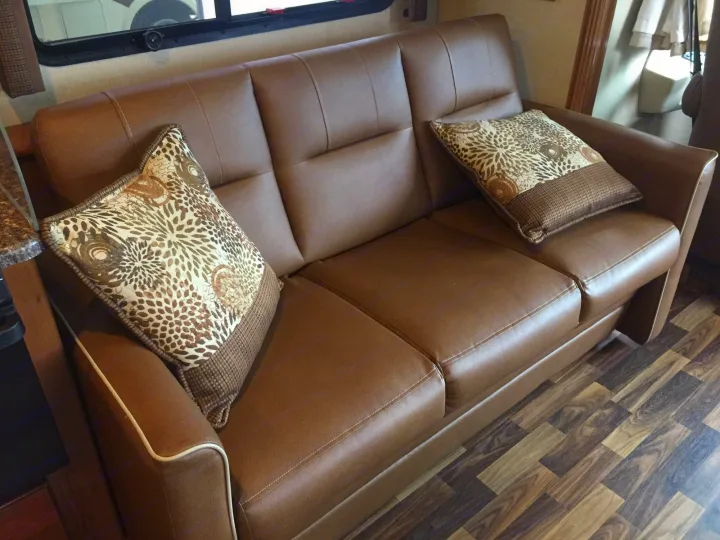 Cozy brown faux leather sofa with decorative throw pillows and wood-look flooring inside an RV rental.. Coachmen Pursuit 2019