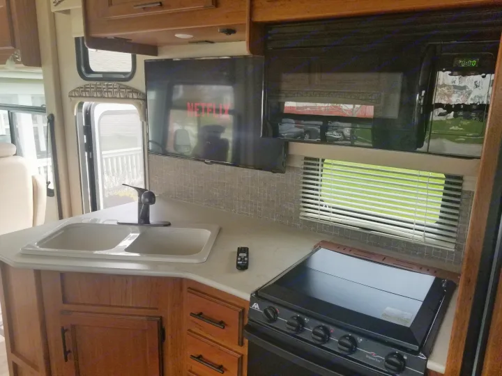 Functional RV rental kitchen featuring a double sink, stove, microwave, and TV. Enjoy home comforts on the road.. Jayco Alante 2016