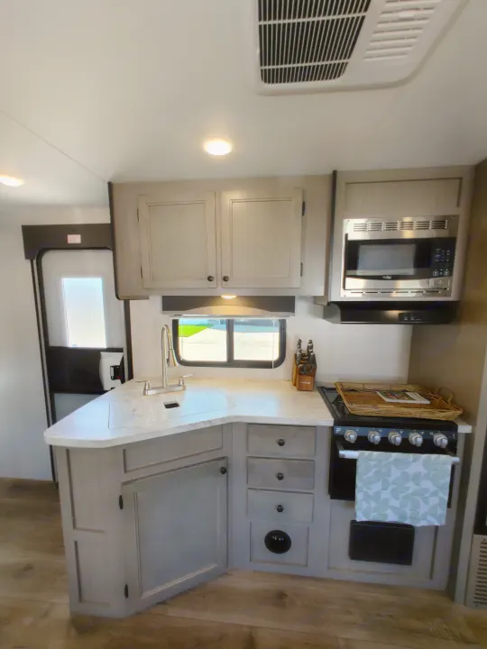 Inside a modern RV rental: a bright kitchen with light-toned cabinets, counter, sink, microwave, and stove for comfortable travels.. Starcraft Travel Trailer 2021