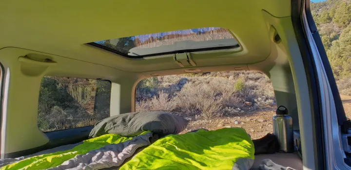 Cozy rv rental interior setup for car camping with a sleeping pad, pillow & bottle. Views of arid outdoor landscape.. Honda Element 2003