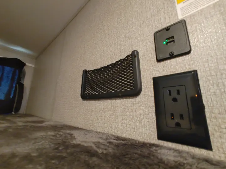 RV rental bunk area: Charging station with USB ports (green lights visible), an electrical outlet, and a mesh storage net for convenience.. Starcraft Travel Trailer 2021