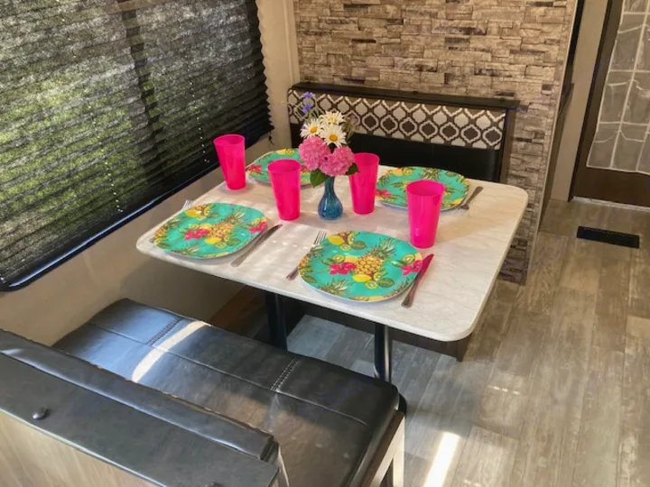 Inside an rv rental: bright dinette with tropical plates, pink cups, and flowers. Ready for compact dining.. Forest River Prime Time Avenger 2021