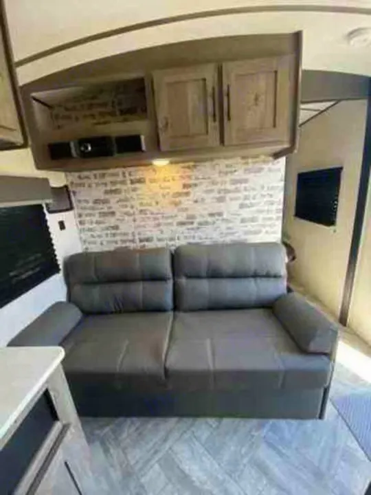 Comfortable RV rental interior with a grey sofa, overhead cabinets, and brick accent wall, perfect for your next adventure.. Keystone Springdale 2021