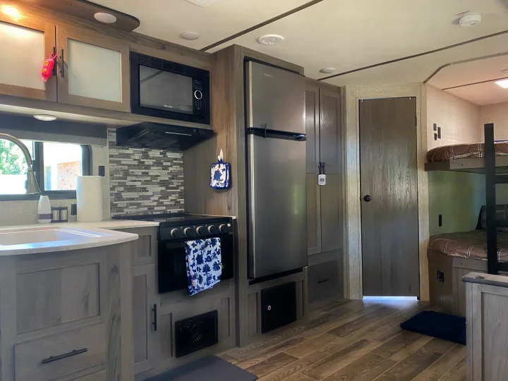 Spacious RV rental interior featuring a modern kitchen area with a sink, microwave, fridge, stove, and comfortable bunk beds.. Gulf Stream Other 2021