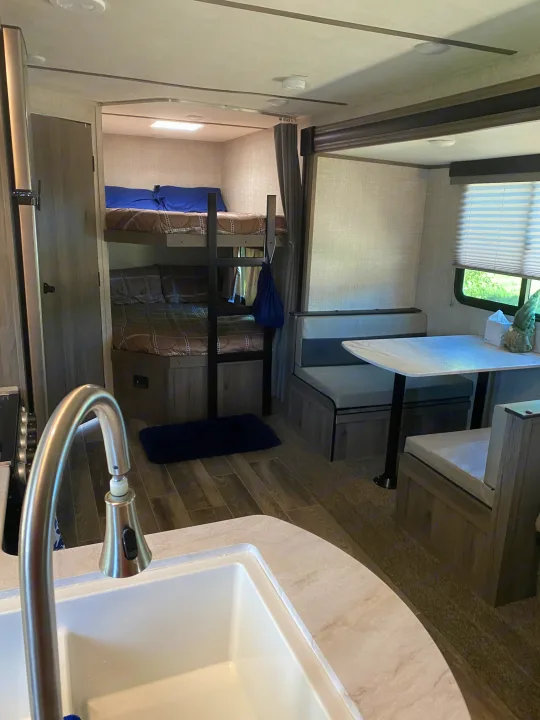 Cozy RV rental interior with a kitchen sink in the foreground, bunk beds, and a dinette area with bench seating.. Gulf Stream Other 2021