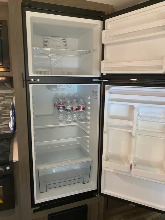 Open RV rental fridge showing empty freezer & shelves. Water bottles are on a shelf in the lower fridge compartment.. Gulf Stream Other 2021