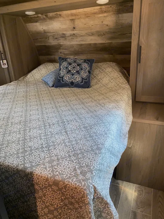 Cozy RV rental bedroom featuring a bed with a gray and white patterned quilt, two pillows, and rustic wooden walls.. Gulf Stream Other 2021