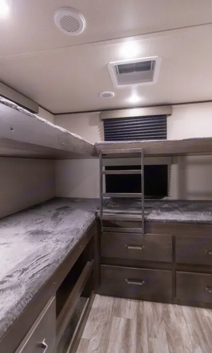 Modern RV rental bunk beds feature plush grey mattresses, a ladder, and built-in storage drawers/shelves.. Grand Design Other 2021