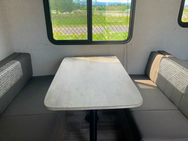 Spacious RV rental dinette with a light-colored table and comfortable upholstered bench seats inside.. Crossroads Zinger 2021