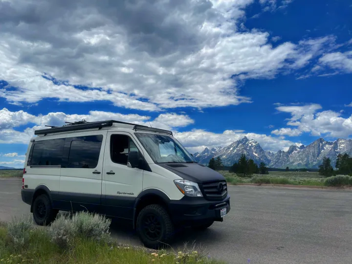 Mercedes Sprinter RV rental parked, facing majestic snow-capped mountains under a cloudy sky. Ideal for adventure travel.. Mercedes Sprinter 2018