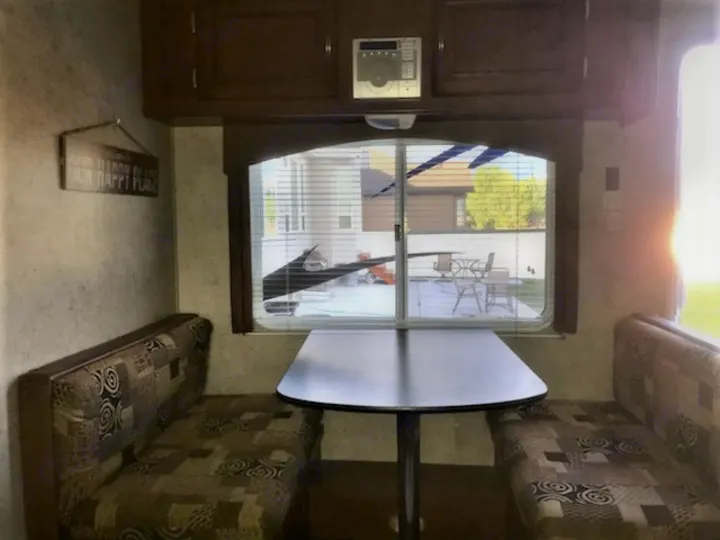 This RV rental interior features a cozy dinette with patterned cushions, a table, and a window looking outdoors.. Forest River Wildwood 2010