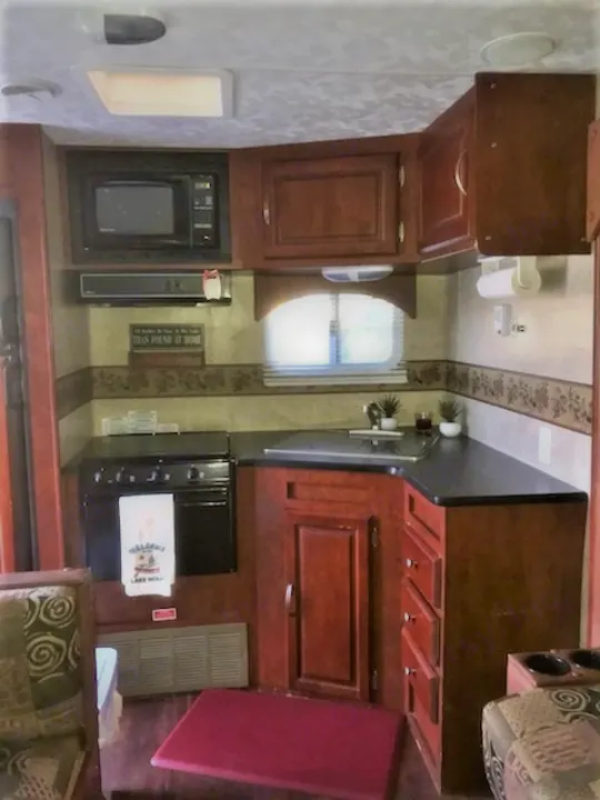 Fully-equipped RV rental kitchen featuring a microwave, stove, sink, and ample wood cabinetry, designed for comfort on the road.. Forest River Wildwood 2010