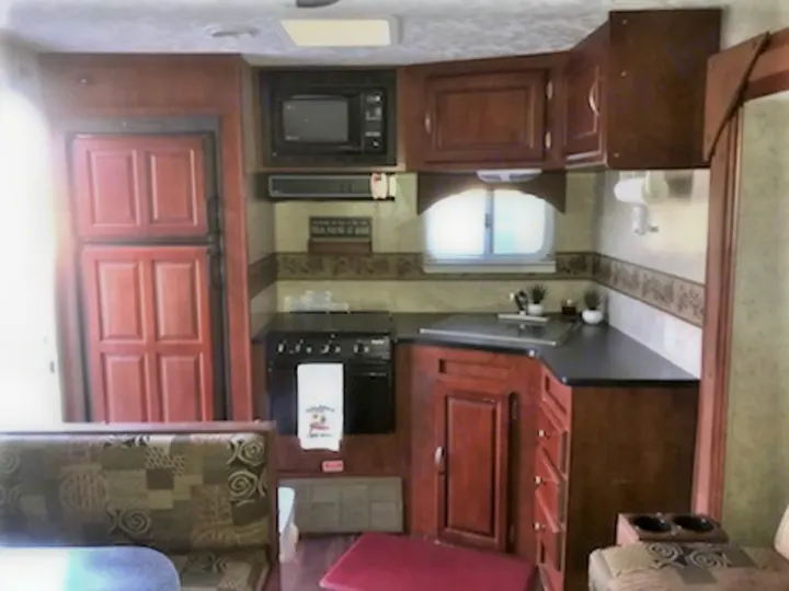 This RV rental features a full kitchen with wooden cabinets, appliances like a microwave, stove, and fridge, plus a dining booth.. Forest River Wildwood 2010