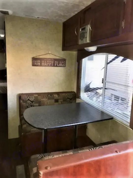 Explore this RV rental's cozy dinette: patterned seating, a table, overhead cabinets, and window with blinds.. Forest River Wildwood 2010