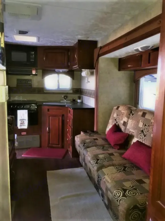 Inside this spacious RV rental: a modern kitchen & cozy living area with a patterned sofa & red pillows.. Forest River Wildwood 2010