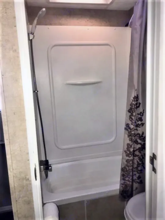 Compact RV rental bathroom with shower/tub combo and handheld showerhead, ideal for travel trailer stays.. Forest River Wildwood 2010