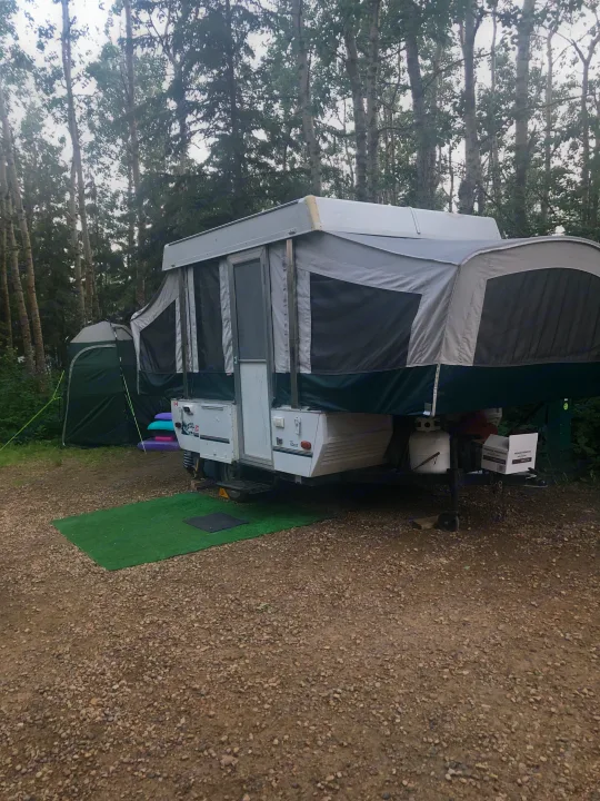 Enjoy the outdoors with this RV rental pop-up camper setup at a wooded campsite, complete with a privacy tent.. Coleman Destiny Taos 1999