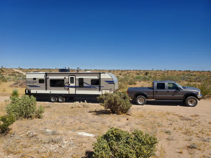 This RV rental, a travel trailer, hitched to a pickup truck, is parked on a dirt road in a sunny desert landscape.. K-Z Manufacturing Sportsmen 2019
