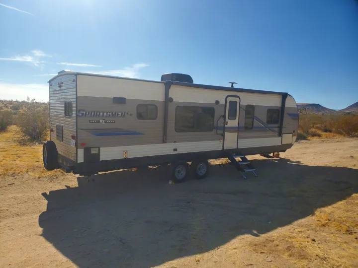 Tan and brown Sportsmen LE RV rental travel trailer parked in a sunny desert landscape with mountains.. K-Z Manufacturing Sportsmen 2019
