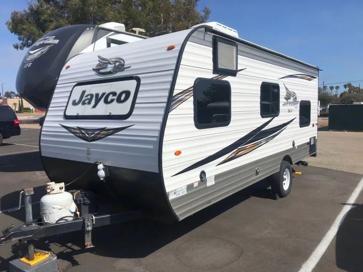 White Jayco Jay Flight SLX travel trailer for rv rental. Parked outside with propane tanks on the hitch, under a clear sky.. Jayco Jay Flight 2019