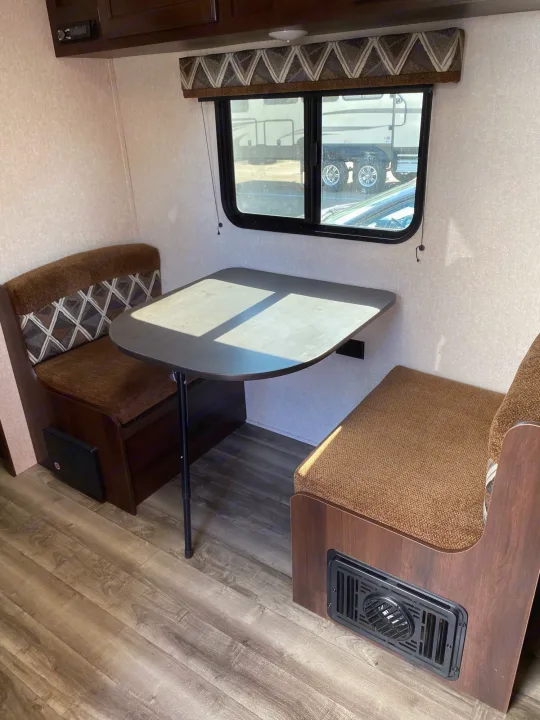 View inside an RV rental: a dinette with brown upholstered benches, a table, and a window with a patterned valance.. Jayco Jay Flight 2019