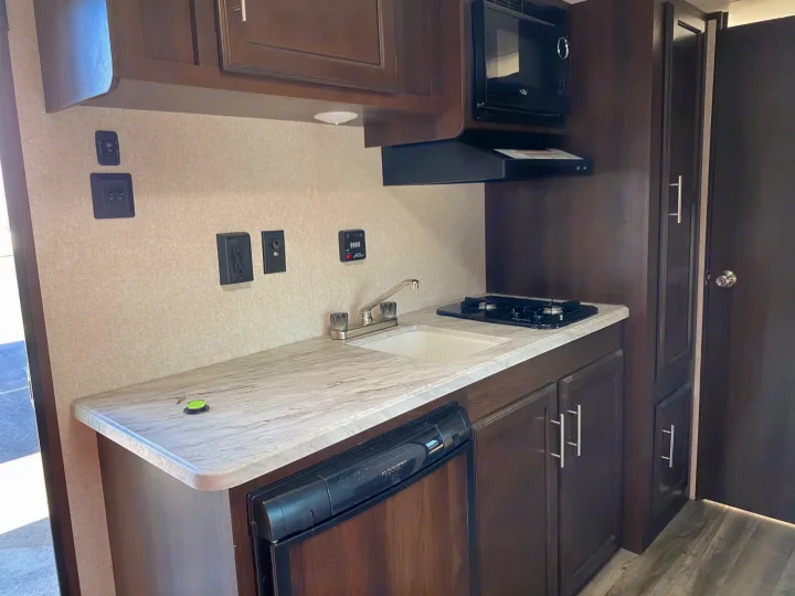 This RV rental shows a compact kitchen with a sink, two-burner stove, microwave, and fridge, all in dark wood cabinetry.. Jayco Jay Flight 2019