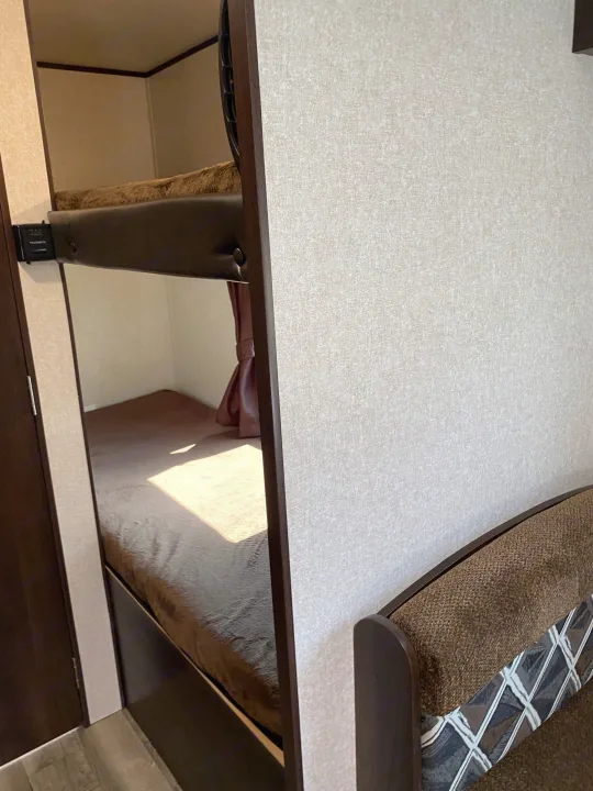 Cozy bunk beds with brown bedding inside an RV rental. Light walls and a dark brown, patterned seating area are visible.. Jayco Jay Flight 2019