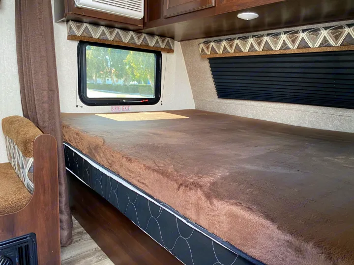 Inside an RV rental: a comfortable bed with a fluffy brown topper, emergency exit window, and pleated blinds.. Jayco Jay Flight 2019
