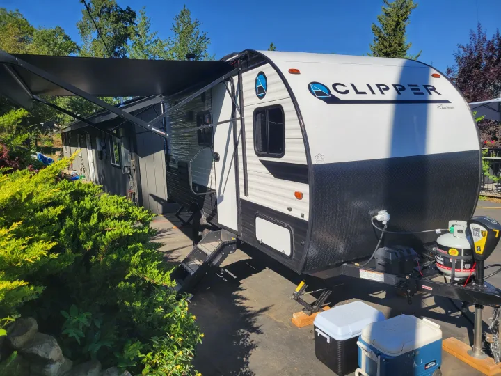 A white Clipper travel trailer RV rental, with its awning extended, is parked outdoors, ready for camping adventures.. Coachmen Clipper 2021
