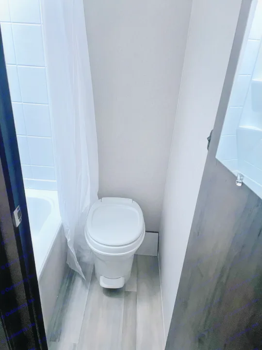 Small, compact bathroom inside an **RV rental** with a white toilet and a tub/shower area with a white curtain. Shows functional space.. Coachmen Clipper 2021