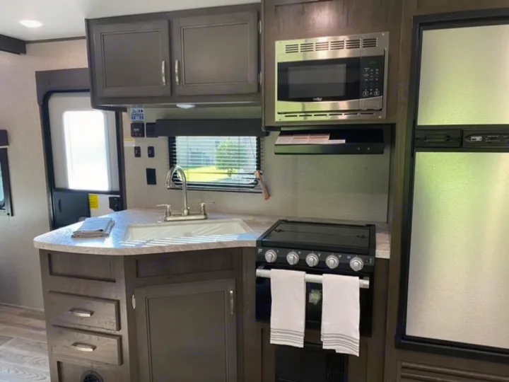 Modern RV rental kitchen features a sink, microwave, stove, and refrigerator, ideal for travel.. Jayco Jay Flight SLX 2021