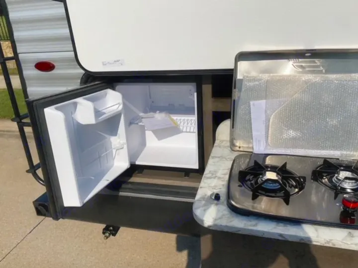 RV rental's outdoor kitchen. Features an open mini-fridge and a two-burner stove on a light marble-patterned countertop.. Jayco Jay Flight SLX 2021