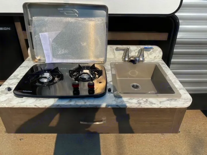 Compact rv rental outdoor kitchen featuring a two-burner stove, sink, and counter, ready for your camping adventures.. Jayco Jay Flight SLX 2021