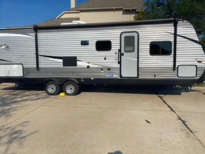 Sleek gray RV rental travel trailer with an awning, parked on concrete with yellow wheel chocks.. Jayco Jay Flight SLX 2021