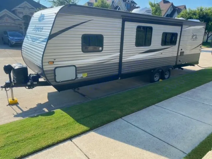 A large, silver Jayco travel trailer, an excellent RV rental option, is parked on a paved residential drive.. Jayco Jay Flight SLX 2021