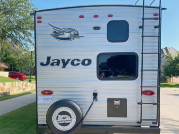Rear view of a silver Jayco travel trailer, an ideal RV rental with a ladder and spare tire. Perfect for road trips.. Jayco Jay Flight SLX 2021