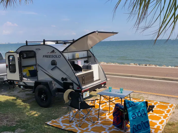 Enjoy beachfront camping with this cozy RV rental. Features an outdoor kitchen and comfy bed, set on a bright mat by the water.. Braxton Creek Free Solo 2021