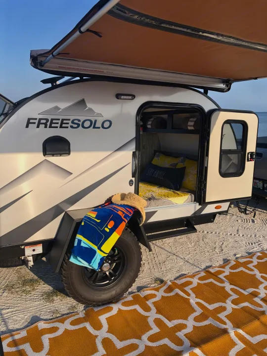 FREESOLO teardrop RV rental set up by the water, awning extended, door open to interior. Perfect for beach camping.. Braxton Creek Free Solo 2021
