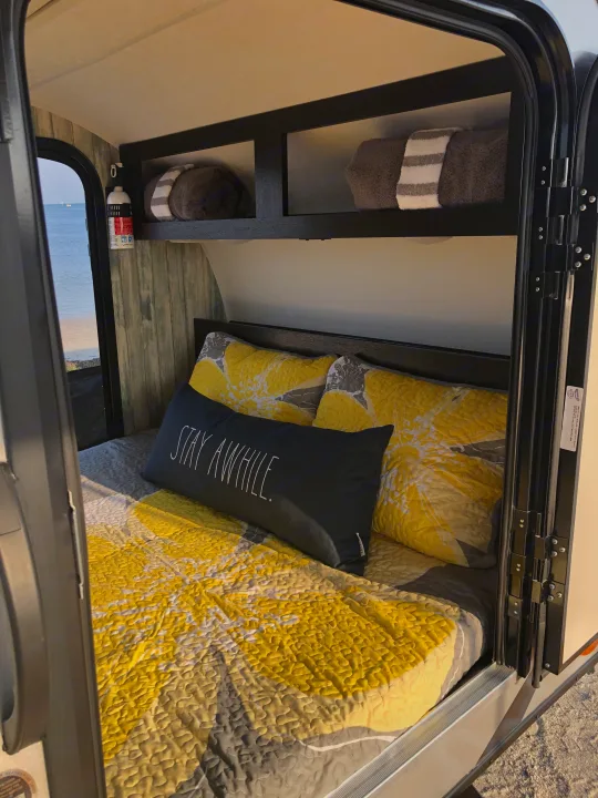 Cozy RV rental interior with yellow bedding and ocean view, featuring a comfortable bed for a relaxing stay.. Braxton Creek Free Solo 2021