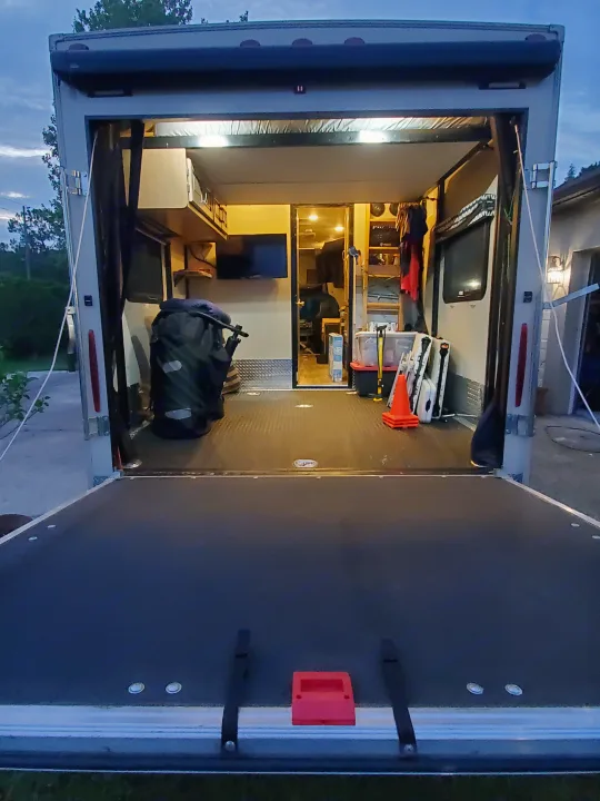 An RV rental toy hauler's lighted interior garage is revealed through its open ramp, showing versatile storage solutions.. Thor Motor Coach Outlaw 2021