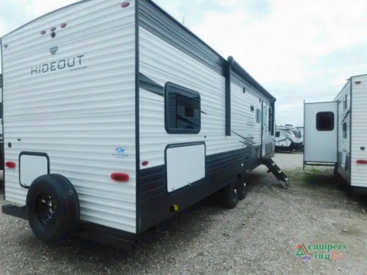 White Keystone Hideout travel trailer RV with spare tire and extended steps on a gravel lot, ready for your RV rental adventure.. Keystone Hideout 2021