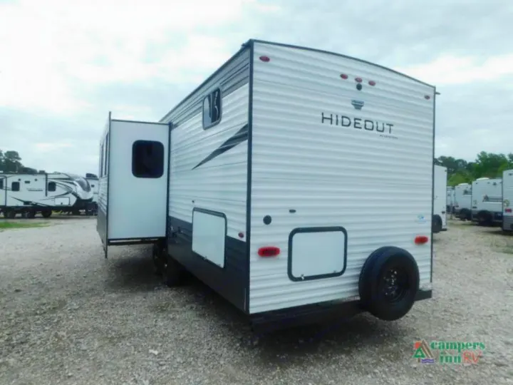 White Hideout travel trailer with extended slide-out, perfect for an RV rental adventure. Parked on gravel.. Keystone Hideout 2021