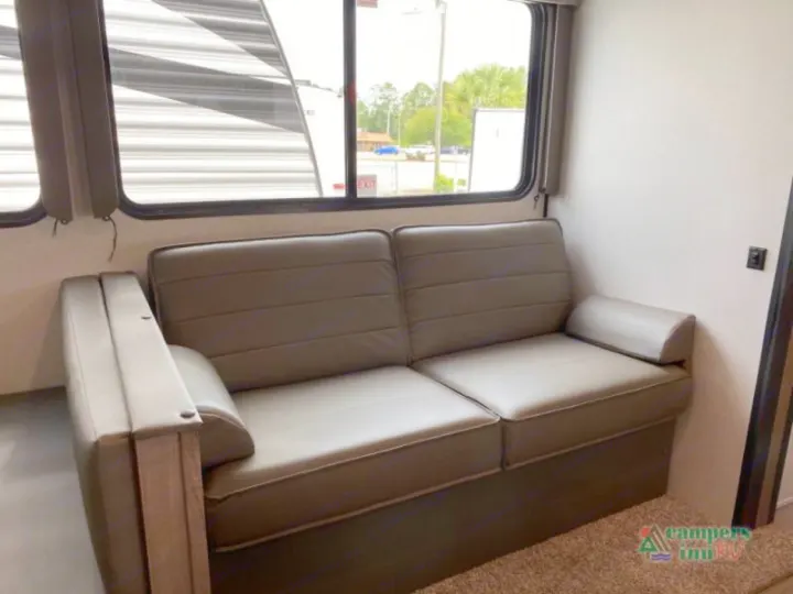 Inside an RV rental: a modern taupe sofa, large windows, and a cozy living space, ideal for travel relaxation.. Keystone Hideout 2021