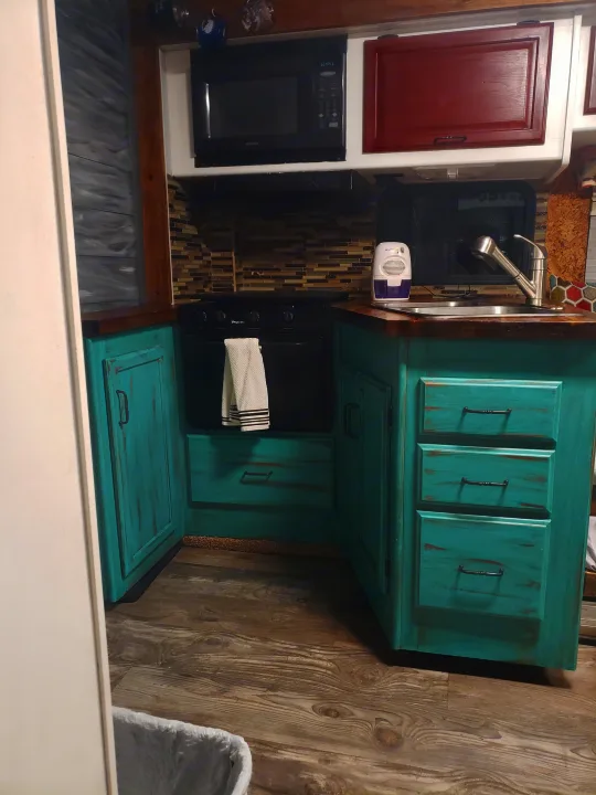 Modern RV rental kitchen featuring distressed teal cabinets, wood counters, black appliances, a sink, and stylish plank walls.. Winnebago Brave 2001