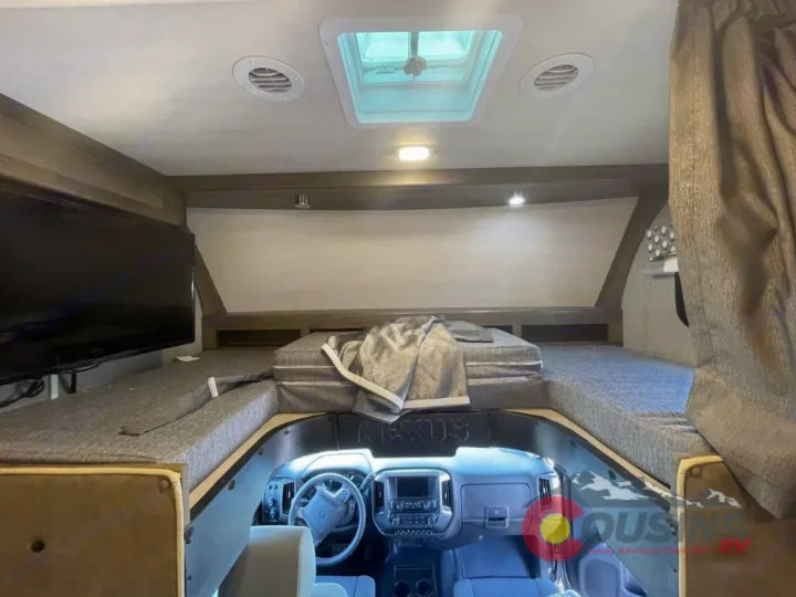 RV rental interior: spacious over-cab bunk bed with TV, skylight, and driver's area view.. Nexus Rebel 2022