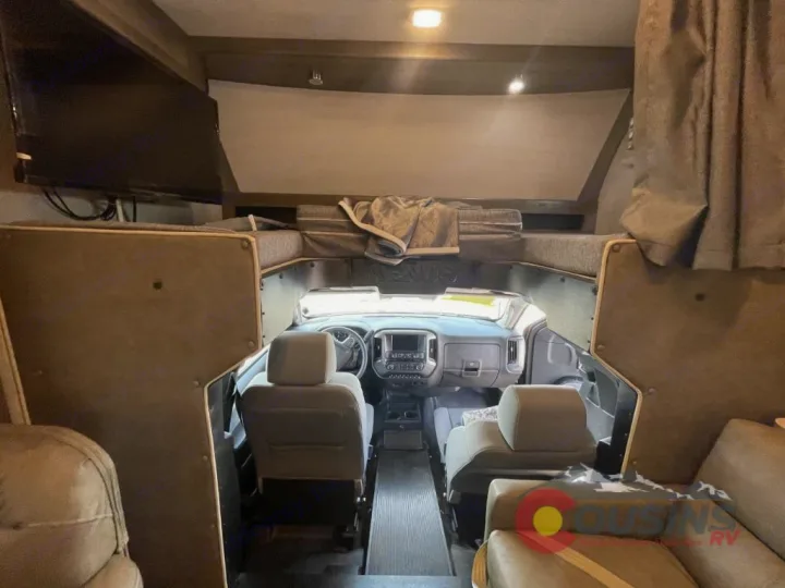 Inside this RV rental: a cozy view of the driver's cab, front seats, and overhead bunk with a TV on the left.. Nexus Rebel 2022