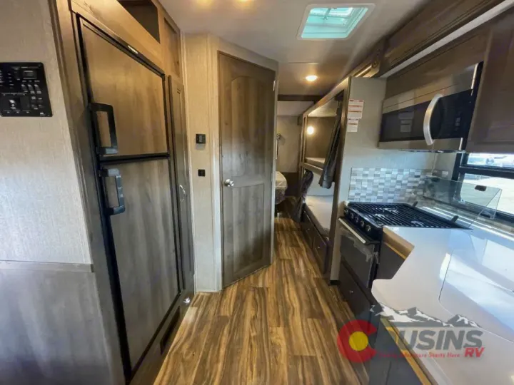 This RV rental interior shows a kitchen (fridge, stove, microwave) on the right, with bunk beds visible further back.. Nexus Rebel 2022
