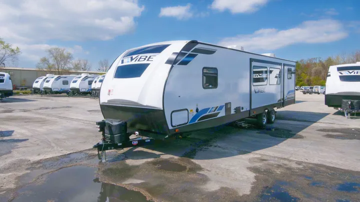 A white and black VIBE travel trailer, one of many RVs parked on a large lot, ready for your next RV rental adventure.. Forest River Vibe 2021