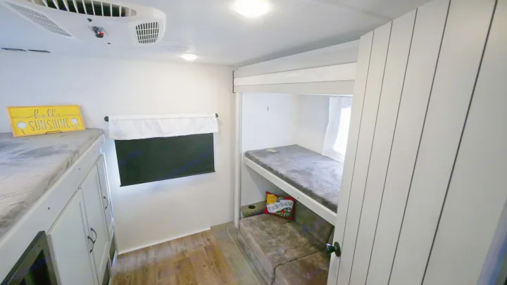 RV rental bunkhouse: two bunks, one with "hello sunshine" sign, another above a sofa bed. AC unit overhead.. Forest River Vibe 2021